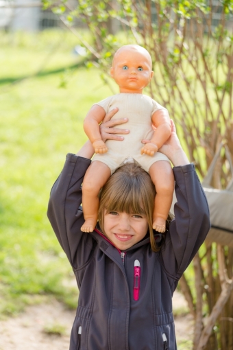 Ein Kind trägt eine Puppe auf dem Kopf und hält sie dabei an den Armen fest