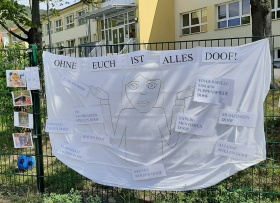 Ein Plakat mit einer Erzieherin und der Aussage "Ohne euch ist alles doof!" gemalt am Zaun einer Kita