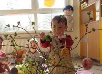 Drei kleine Kinder hängen bunte Ostereier auf einen Strauß auf