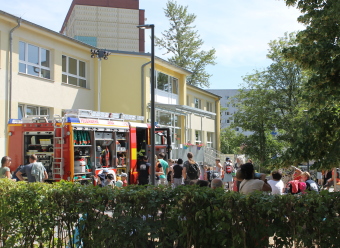 Auf dem Bild sind mehrere Menschen neben einem Feuerwehrauto im Garten zu sehen