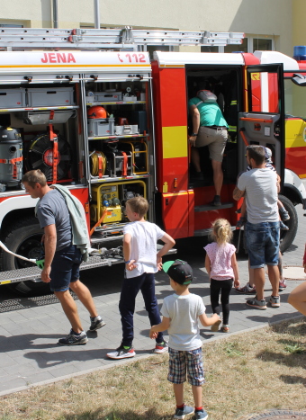 Auf dem Bild sind Erwachsene und Kinder vor einem Feuerwehrauto zu sehen