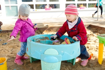 Zwei Kinder spielen mit Matsch und Sand im Sandkasten
