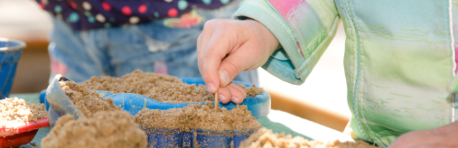 Zwei Kinder spielen mit Sand. Sie backen damit Kuchen.