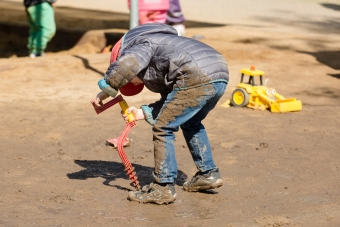 Ein Kind spielt im nassen Sand, seine Hose und Jacke sind schon ziemlich schmutzig