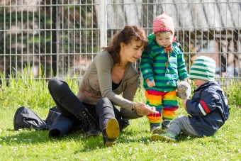 Eine Erzieherin sitzt im Gras und zeigt zwei Kindern einen Gegenstand