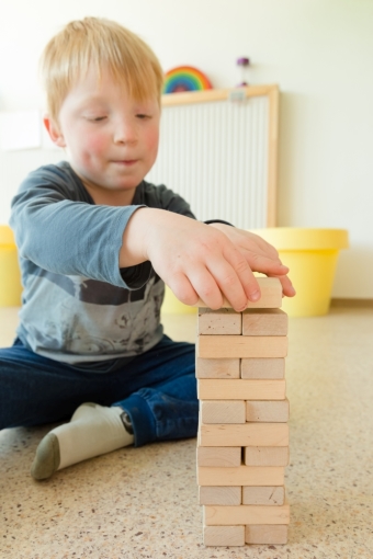 Ein Kind konstruiiert aus Bausteinen einen Turm und legt dabei gerade den nächsten Stein oben auf