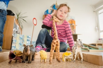 Im Vordergrund stehen sechs Plastiktiere, im Hintergrund sieht man ein Kind, dass mit Bausteinen einen kleinen Zoo gebaut hat