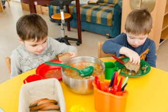Zwei Kinder sitzen am Tisch und essen Gemüsesuppe