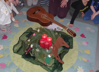 Ein Adventskranz und eine Gitarre im Kreis der Kinder am Teppich